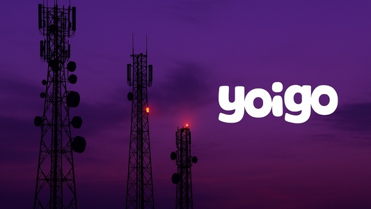 Antenas de telecomunicaciones apagándose al atardecer con el logotipo de Yoigo en primer plano.